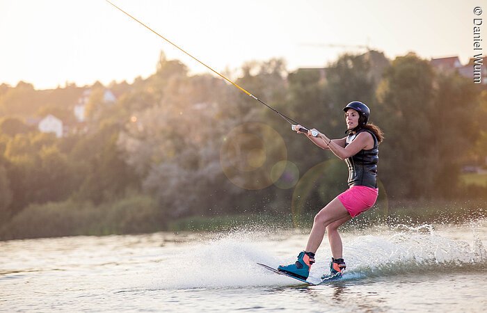 Wakeboardanlage Eine junge Frau gleitet mit ihrem Wakeboard über den See.