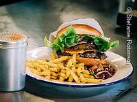 Burger mit Pommes Ein Hamburger mit Pommes auf einem weißen Teller. Der Teller steht auf einer schwarzen Tischplatte.