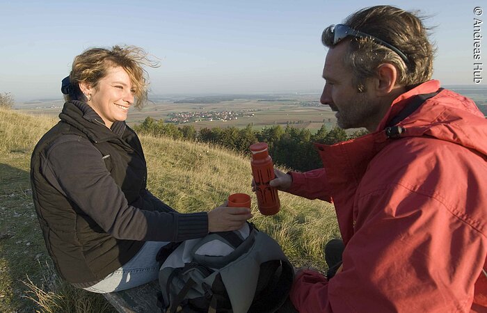 Der Seenländer Frau und Mann stoppen und trinken im Herbst einen heißen Tee auf einer gelen Wiese.